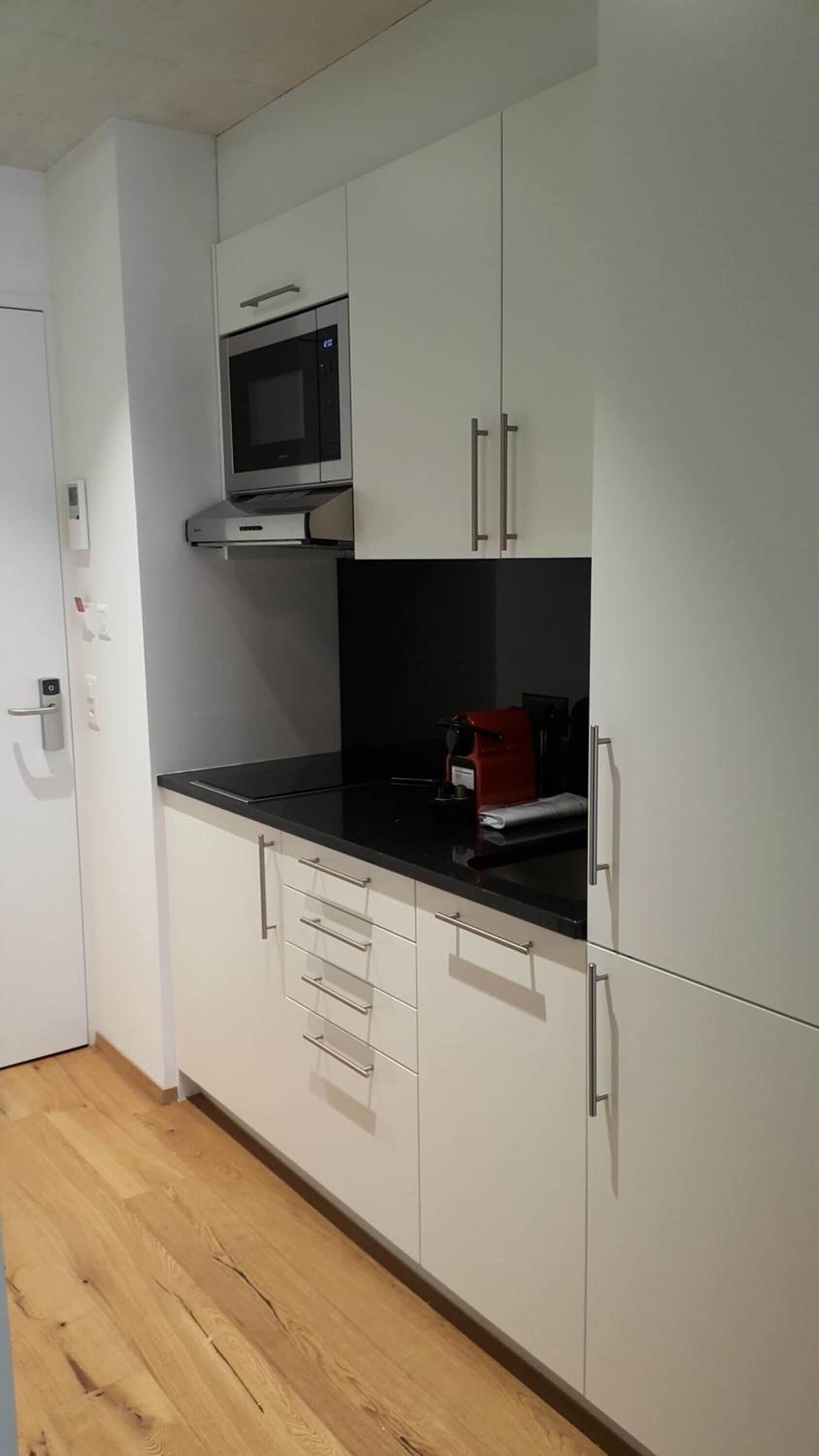 A modern kitchen with white cabinets, a black countertop, a microwave, and a red coffee machine.