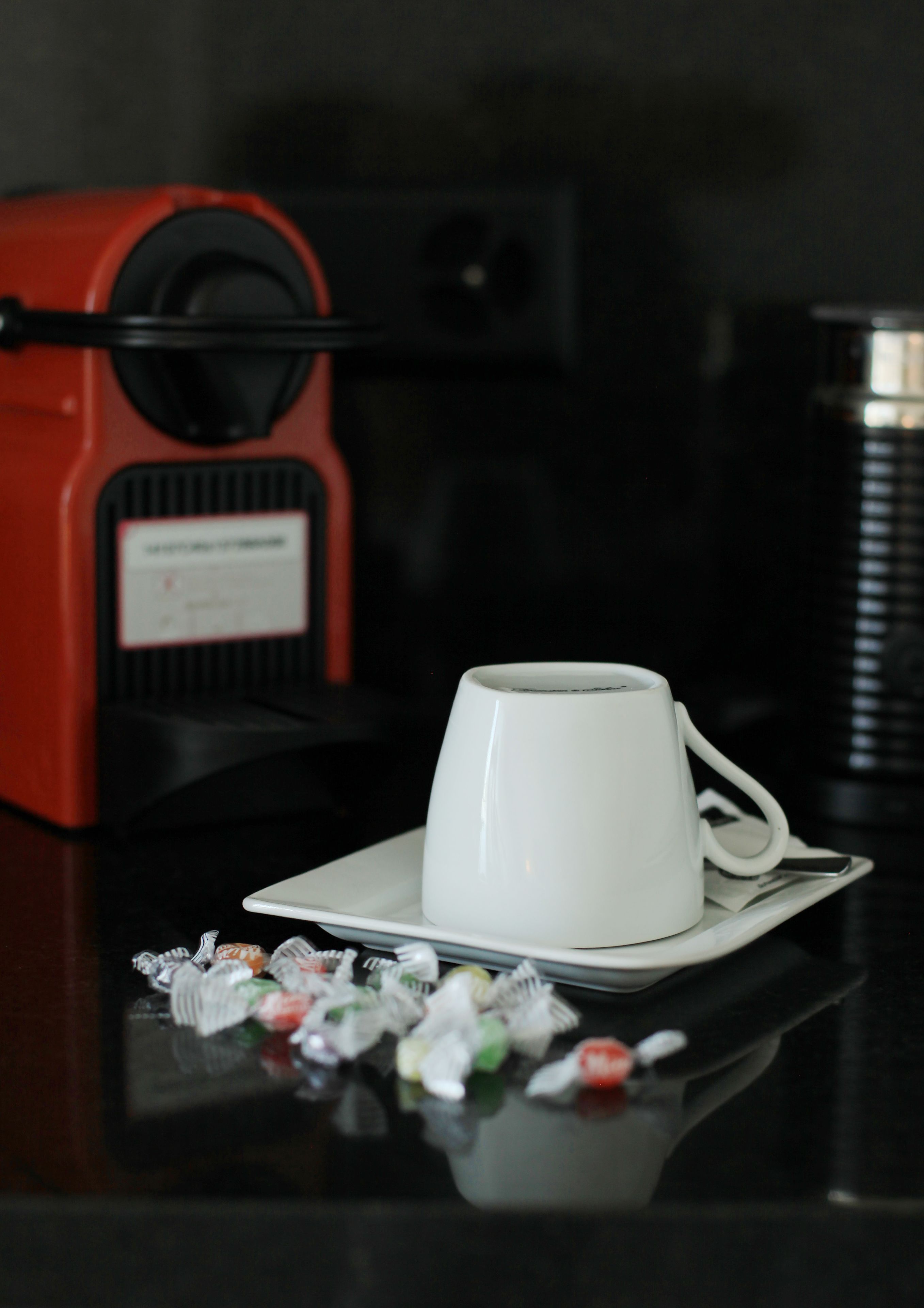 A white cup on a saucer with a red coffee machine in the background.