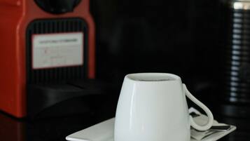 A white cup on a saucer with a red coffee machine in the background.