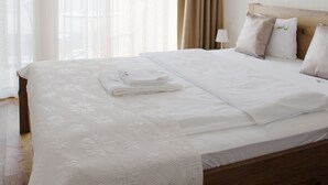 Een keurig opgemaakt bed met witte lakens, een houten hoofdbord en een raam met dunne gordijnen.