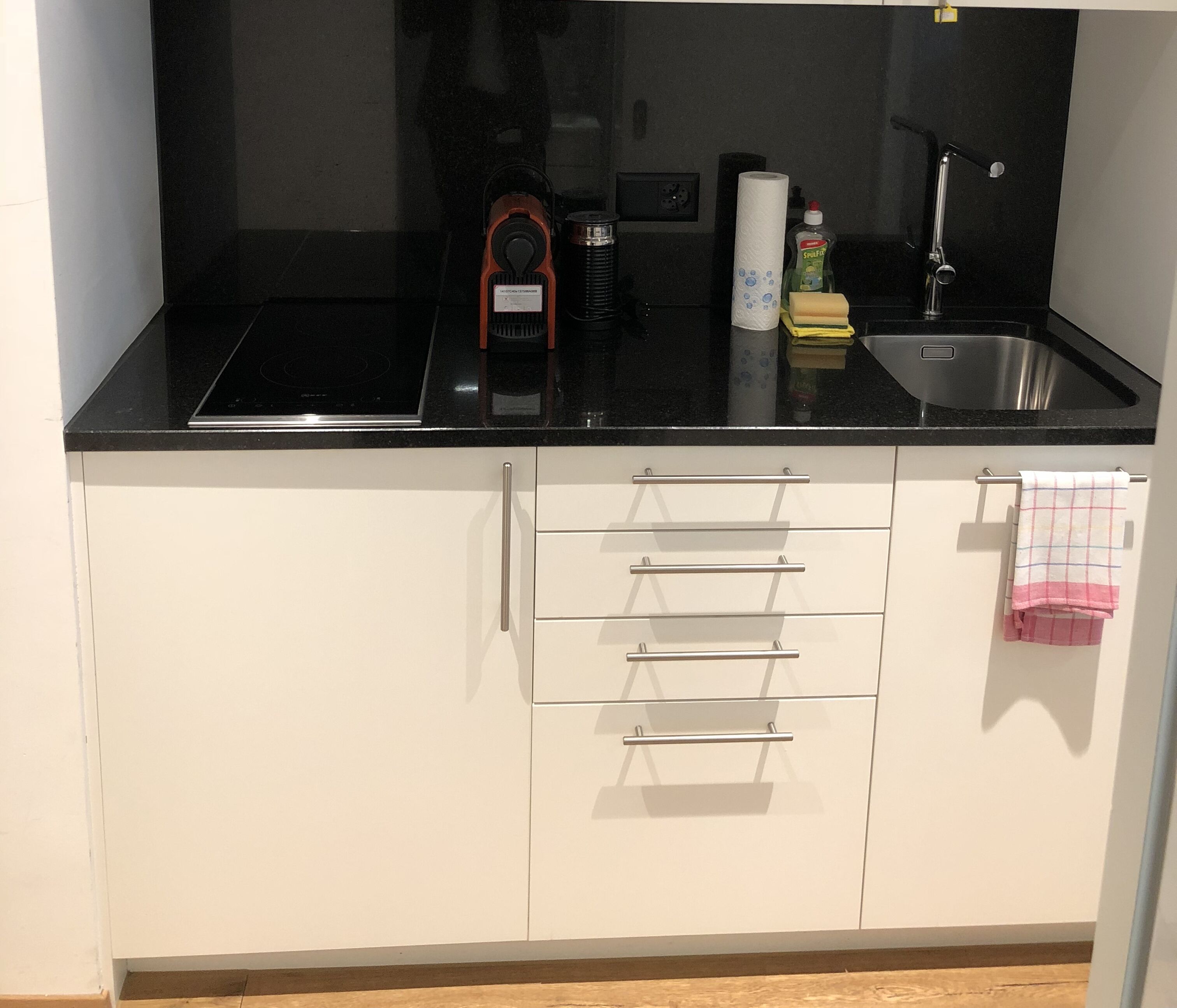 A kitchen with a black countertop, white cabinets, a stainless steel sink, and a towel hanging on the right side.