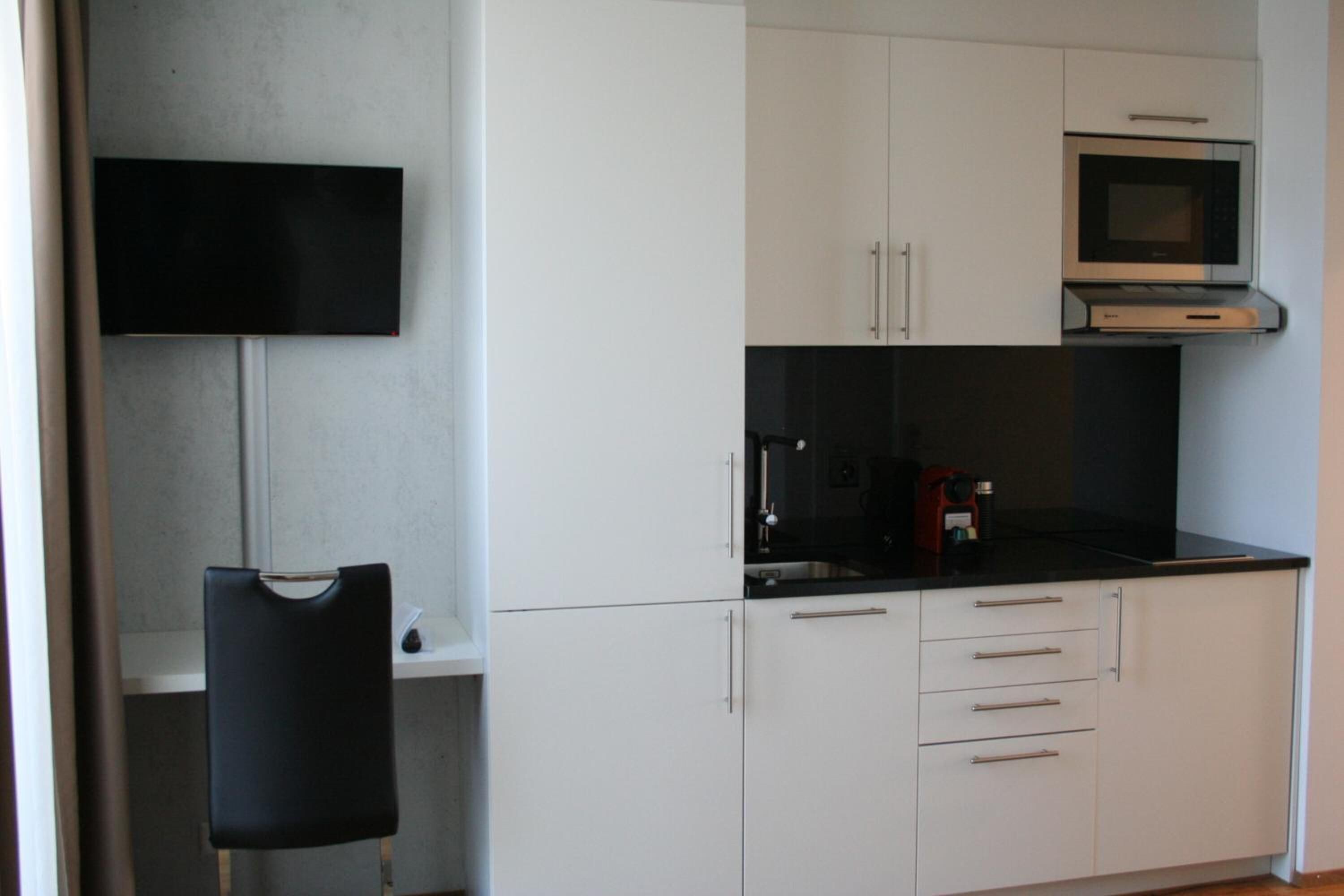 Una cucina moderna con mobili bianchi, un piano di lavoro nero e un forno a microonde integrato.