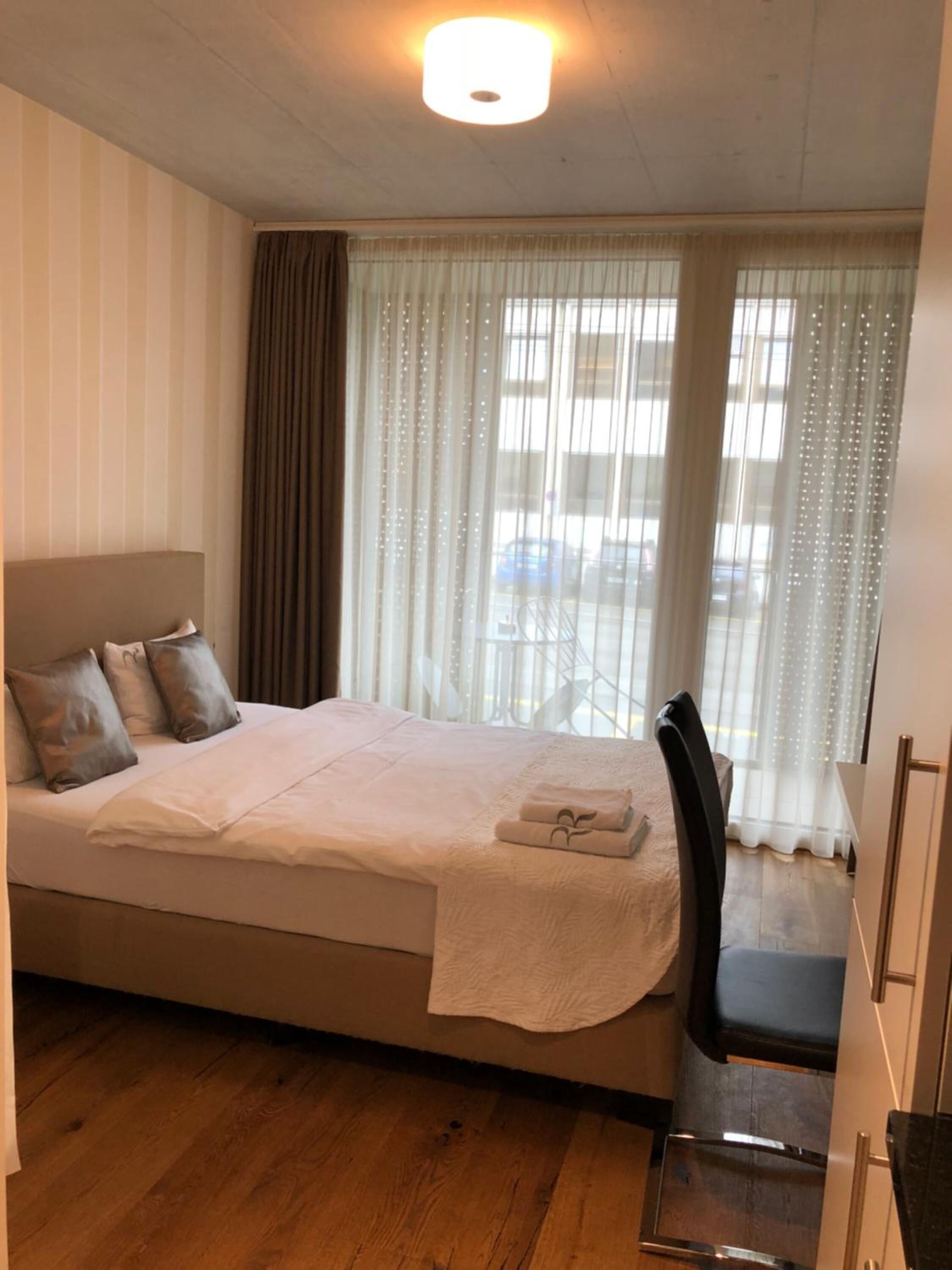 Et hotelværelse med seng, stol, skrivebord og et vindue med gardiner.