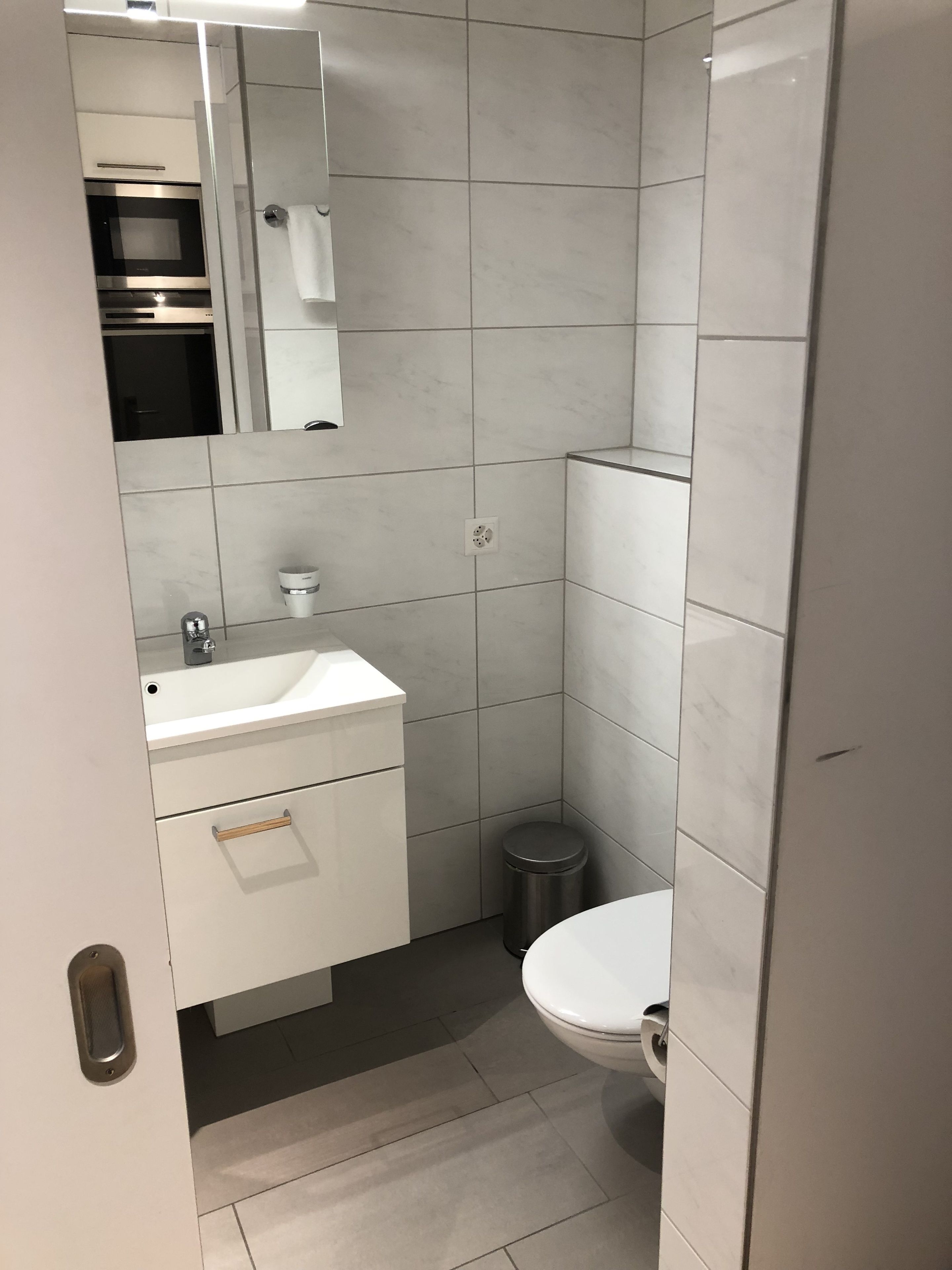 Un baño moderno con lavamanos, espejo e inodoro blancos.