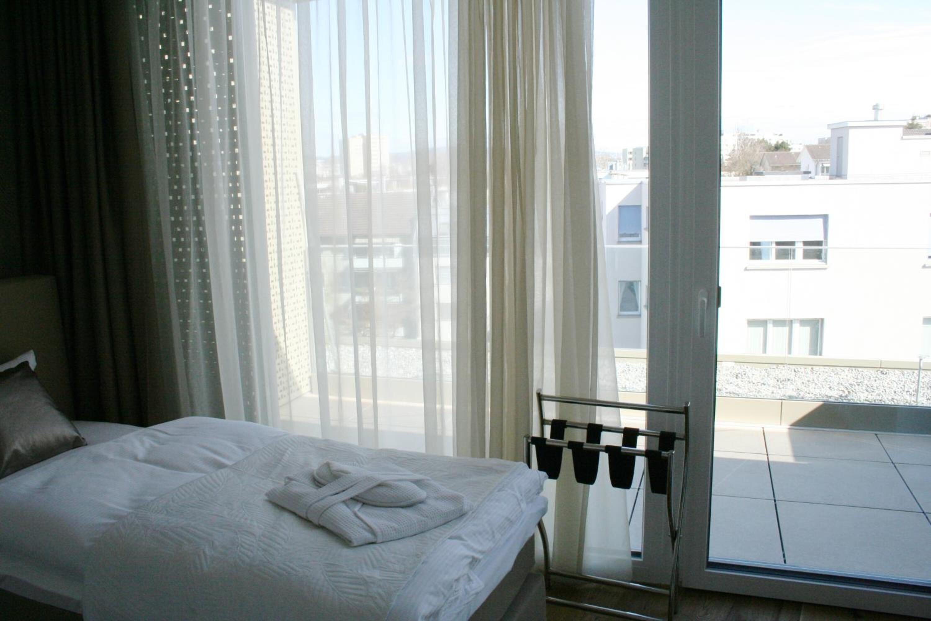 Une chambre d’hôtel avec un lit, une fenêtre avec des rideaux légers et une vue sur les bâtiments environnants.