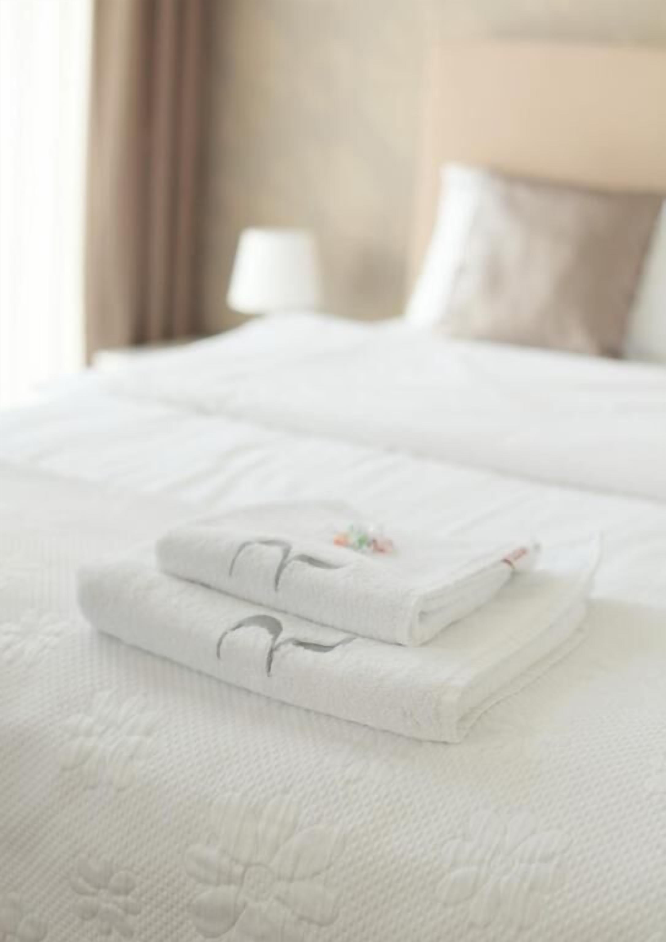 A neatly made bed with folded white towels and a decorative pillow.
