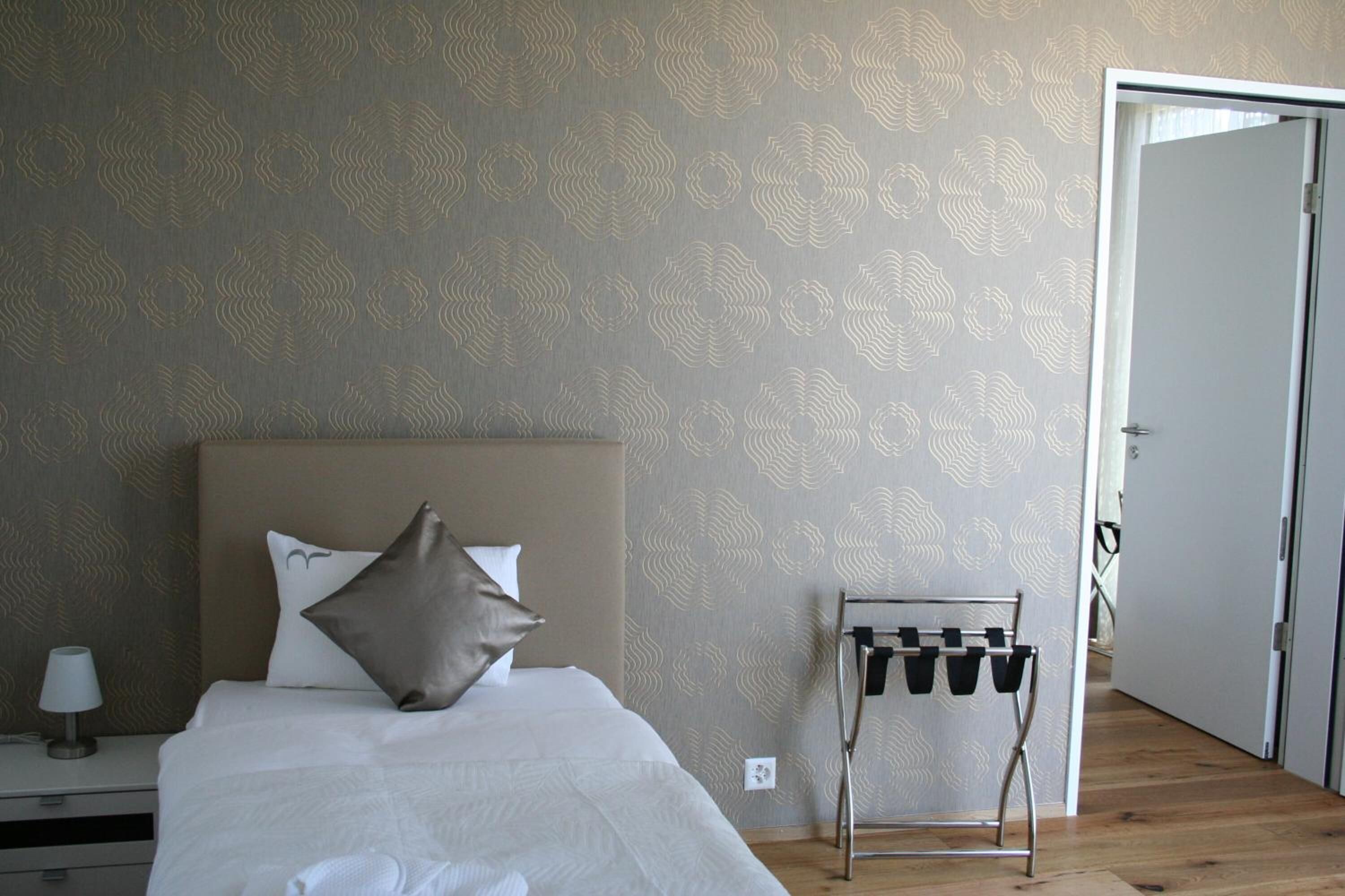 A neatly made bed with a headboard, a bedside table with a lamp, and a wall-mounted coat rack.