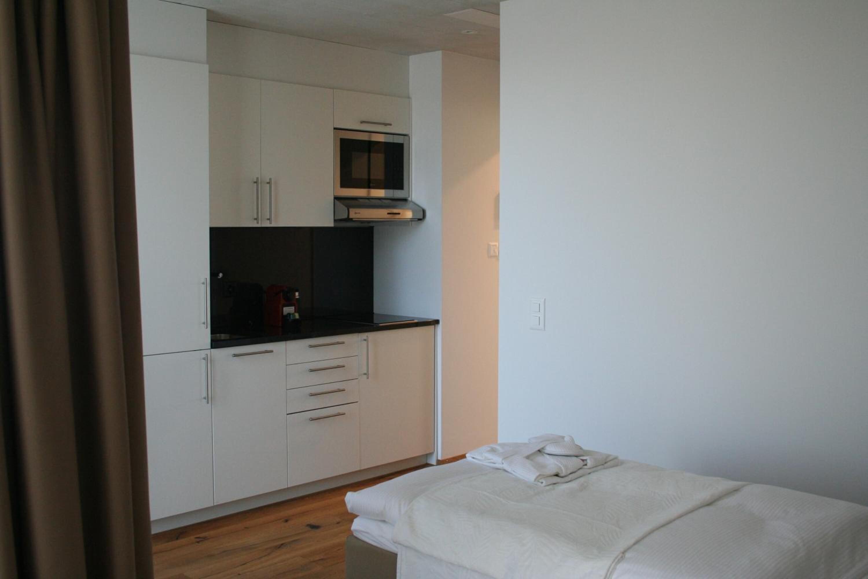 Una habitación pequeña y moderna con kitchenette, cama y cortina.