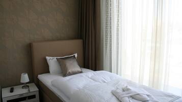 A neatly made bed with white linens and a folded towel, a bedside lamp, and a remote control on a nightstand.