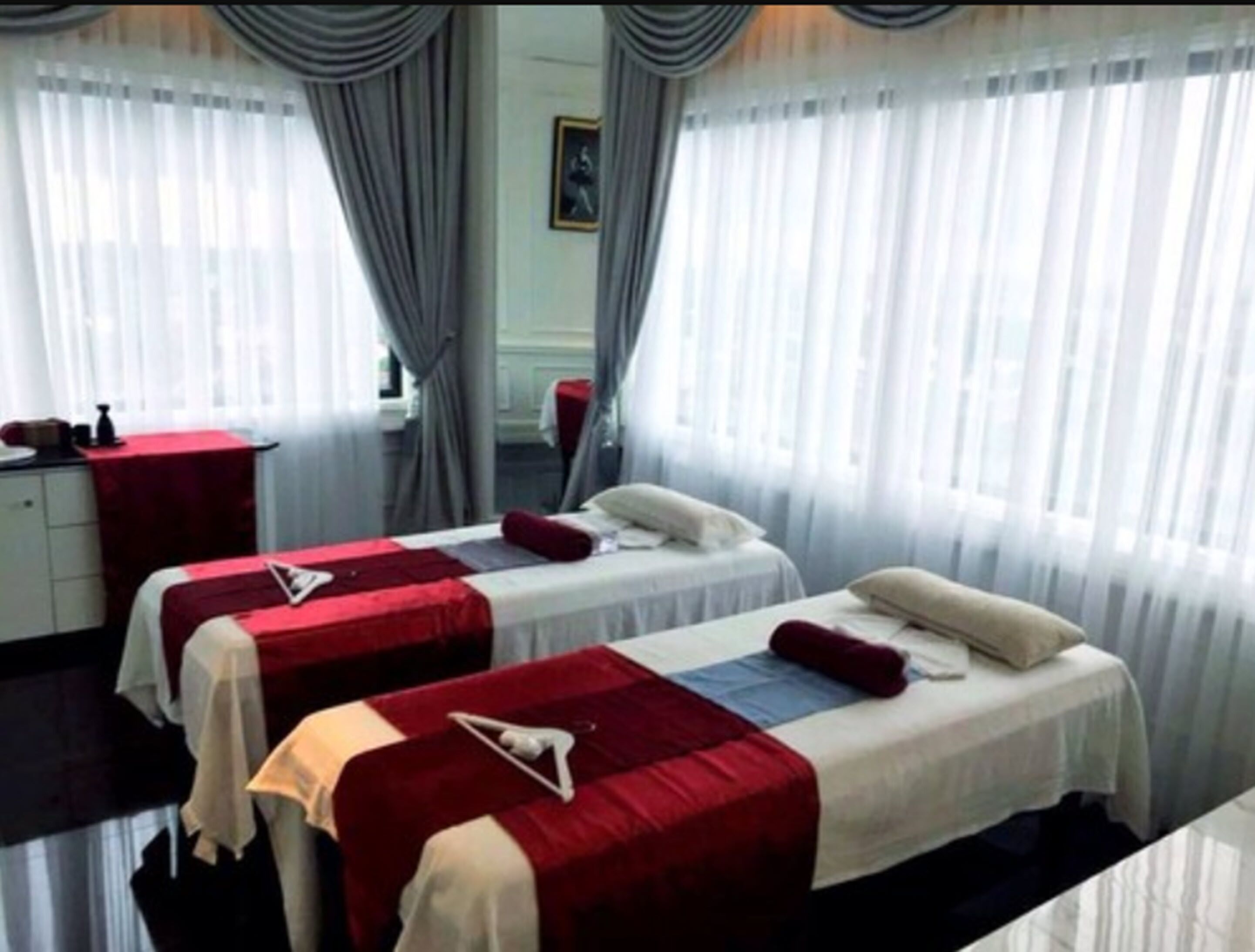 A hotel room with two beds, each with a red and white bedspread, a small table with a red tablecloth, and a mirror on the wall.