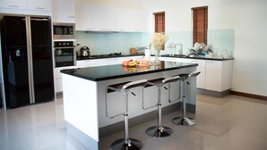A modern kitchen with a central island, bar stools, stainless steel appliances, and a backsplash. - Tulip House Pool Villa Hua Hin (Cha-am)