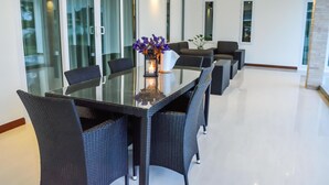 A modern dining area with a glass table surrounded by wicker chairs, a candle centerpiece, and a sofa in the background. - Tulip House Pool Villa Hua Hin (Cha-am)