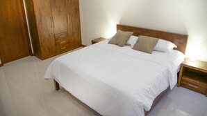 A bedroom with a large bed, wooden wardrobe, and bedside tables. - Tulip House Pool Villa Hua Hin (Cha-am)