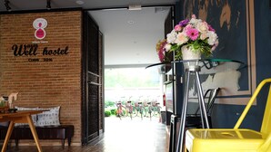 L’intérieur d’une auberge de jeunesse, avec un mur en briques, une table en bois, un canapé, une table en verre ornée de fleurs, et des vélos à l’extérieur.