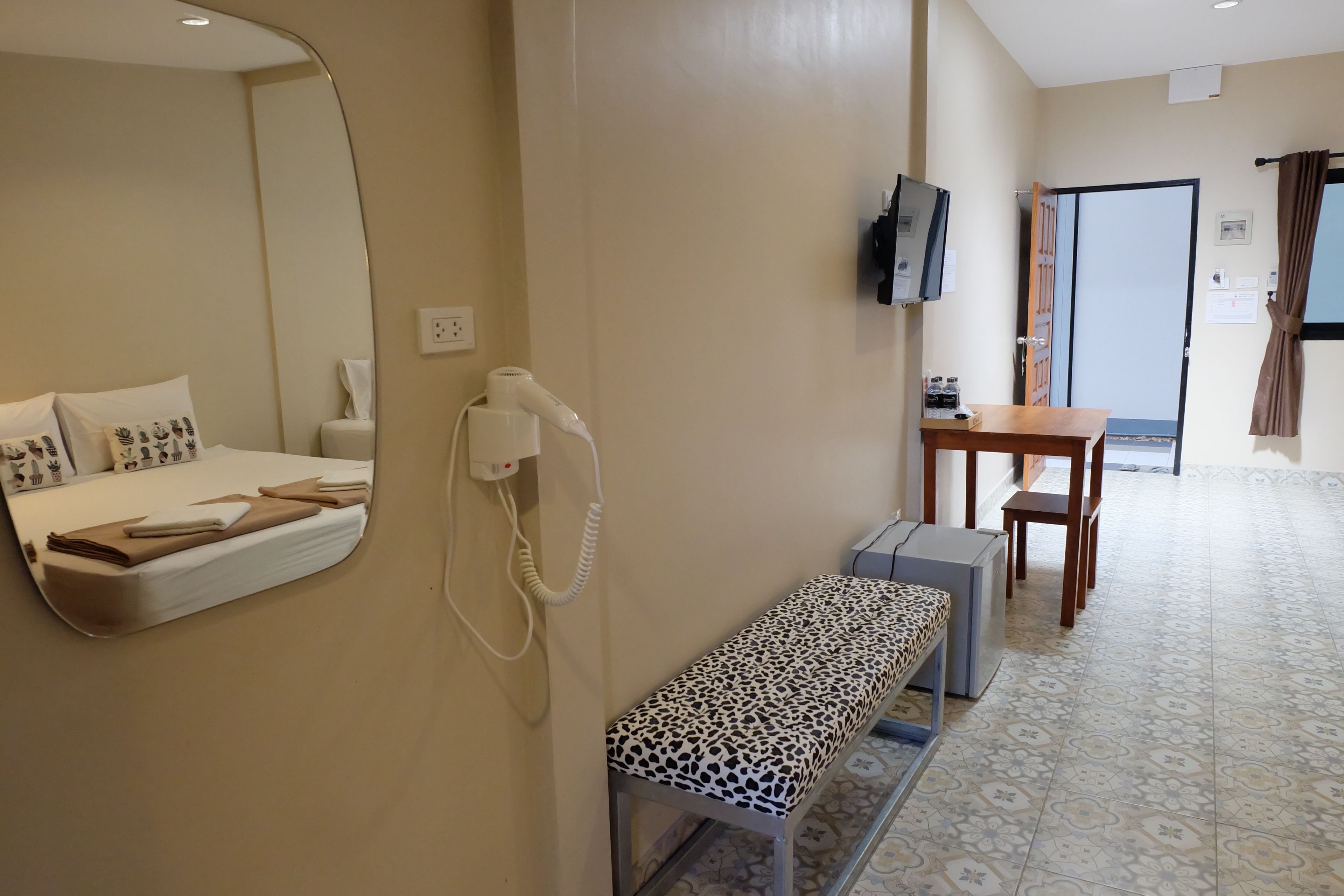 Ein Hotelzimmer mit Bett, einer Bank, einem Schreibtisch, einem Fernseher und einer Badezimmertür.