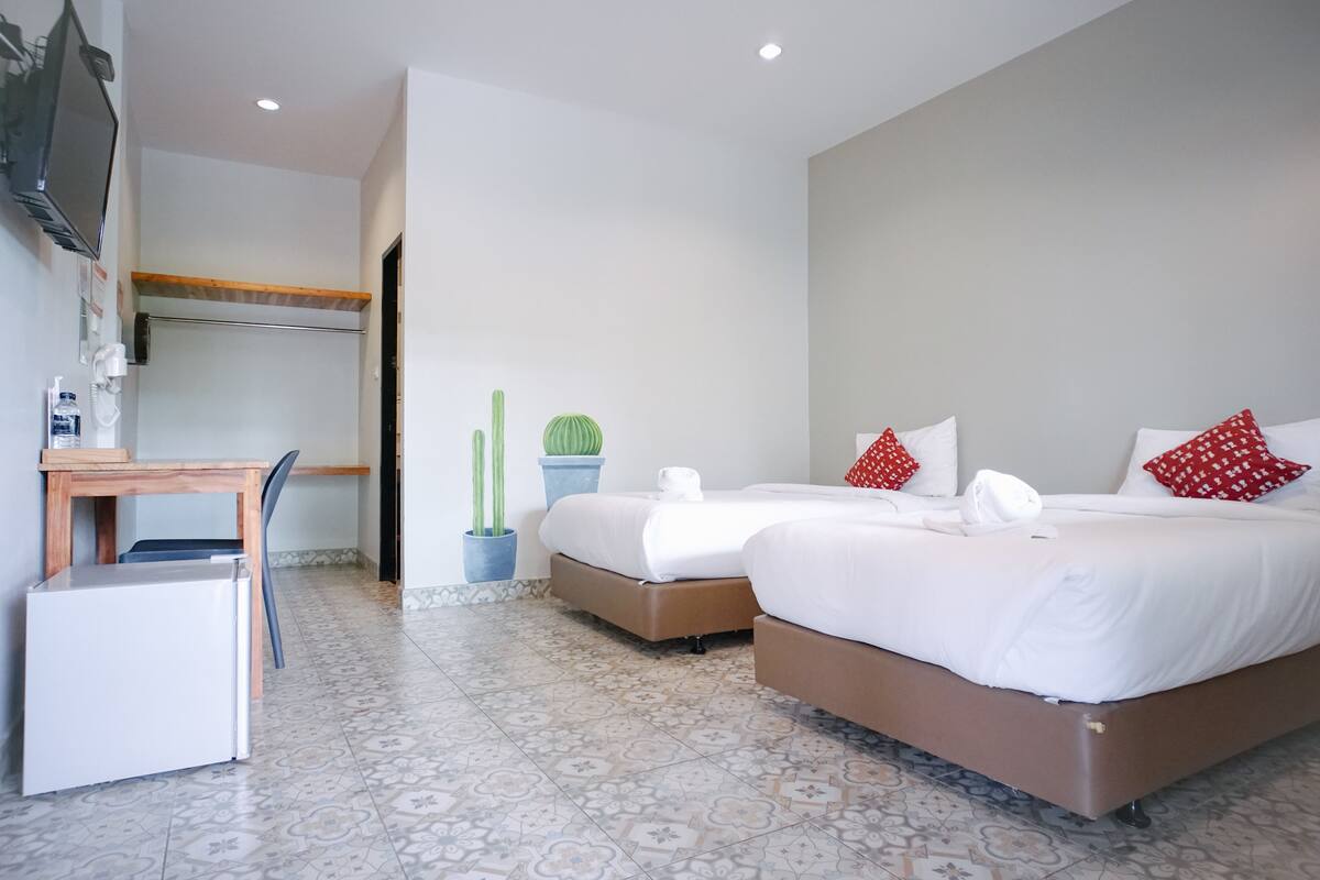 Une chambre d’hôtel avec deux lits, un bureau, un réfrigérateur et des plantes en pot.