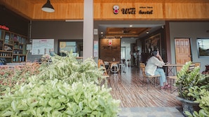 L’intérieur d’une auberge de jeunesse, avec un plafond en bois, des plantes d’intérieur et une personne assise à une table.