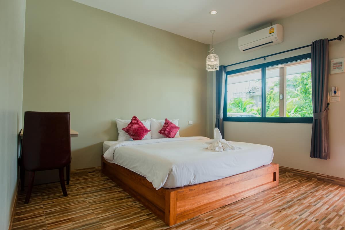 Une chambre à coucher avec un lit en bois, une chaise, une fenêtre avec des rideaux et un appareil de climatisation.