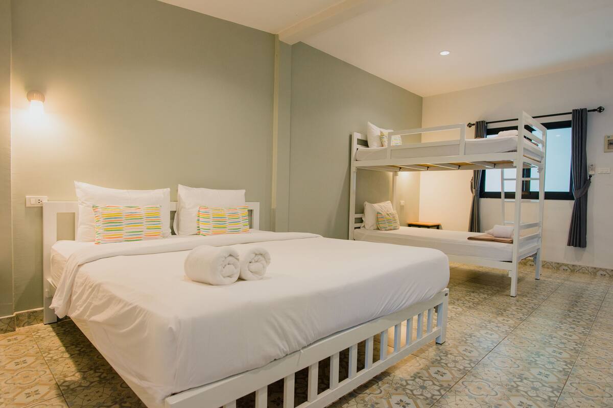 Une chambre d’hôtel avec un grand lit, un lit superposé et une fenêtre avec des rideaux.