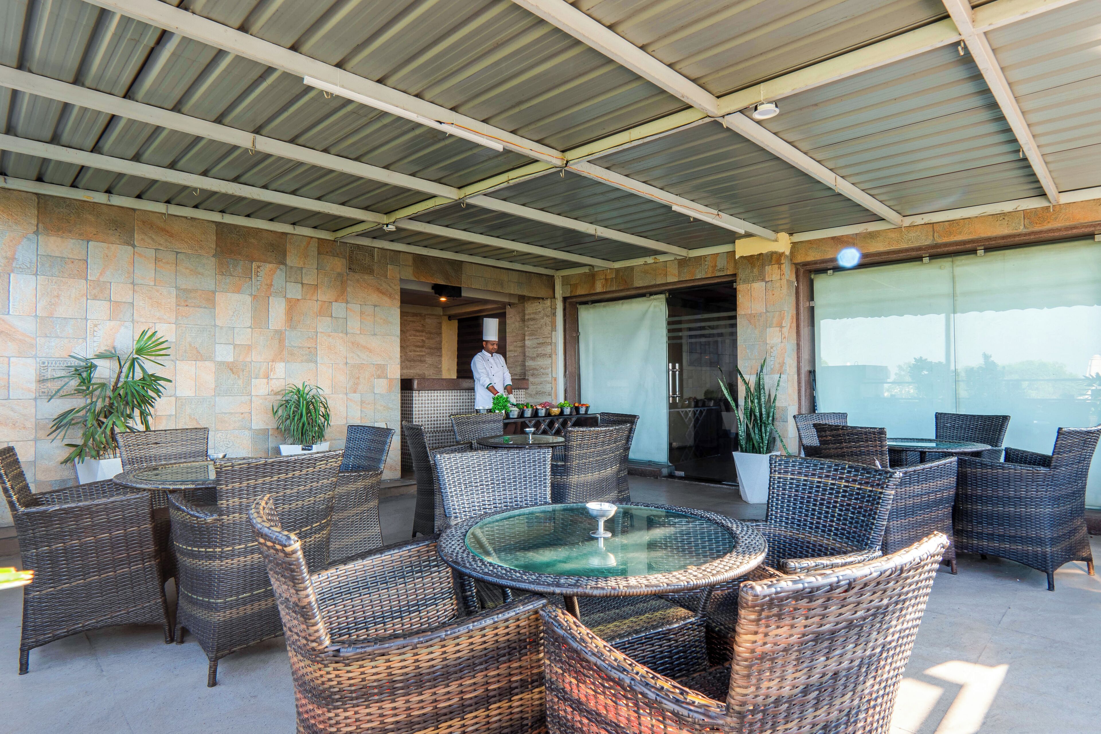 An outdoor patio with wicker furniture, a glass table, and potted plants.