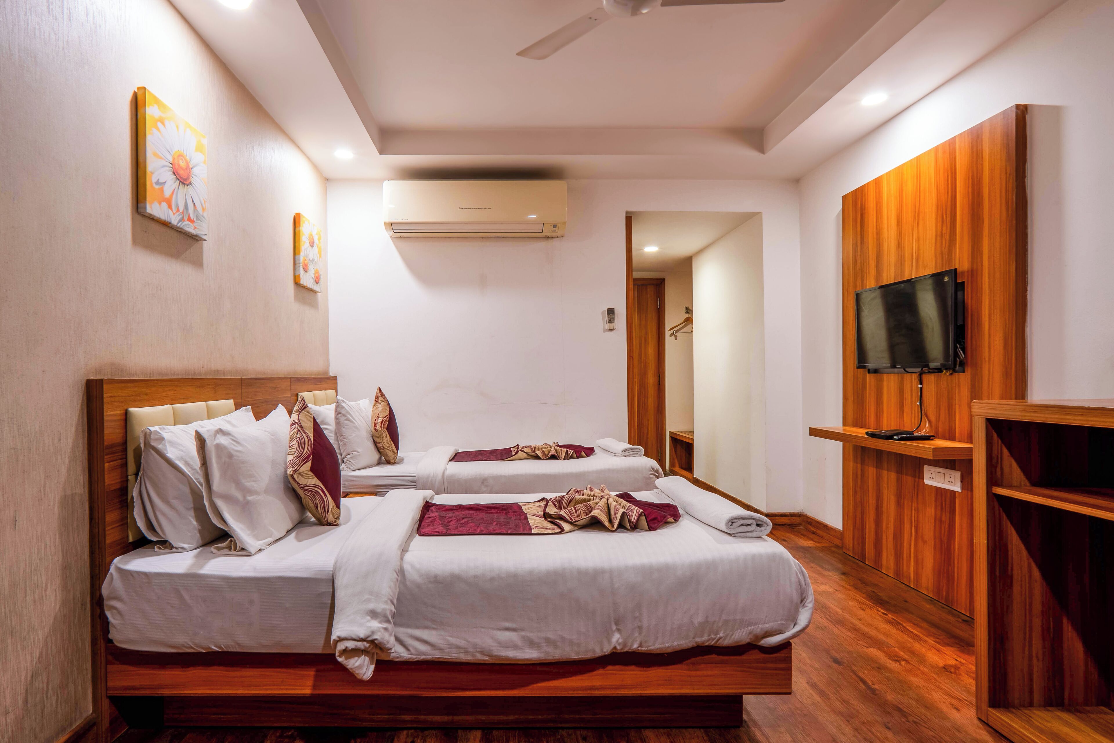 A hotel room with two beds, a TV, and an air conditioning unit.