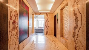 A marble-floored hallway with a large artwork on the left, a staircase in the center, and a patterned wall on the right. - Le Roi Jammu (Jammu)