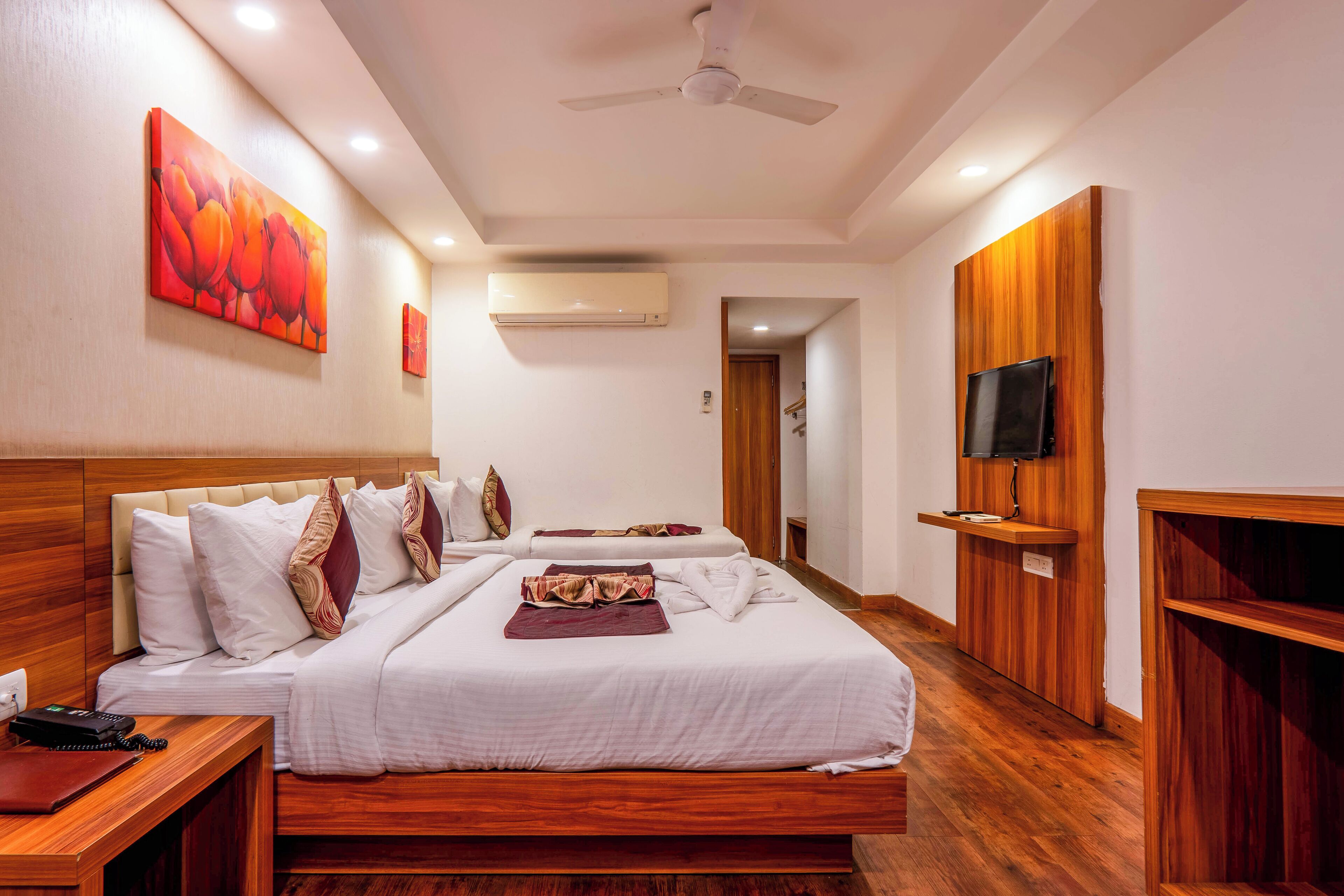 A hotel room with two beds, a TV, an air conditioning unit, and wooden paneling.