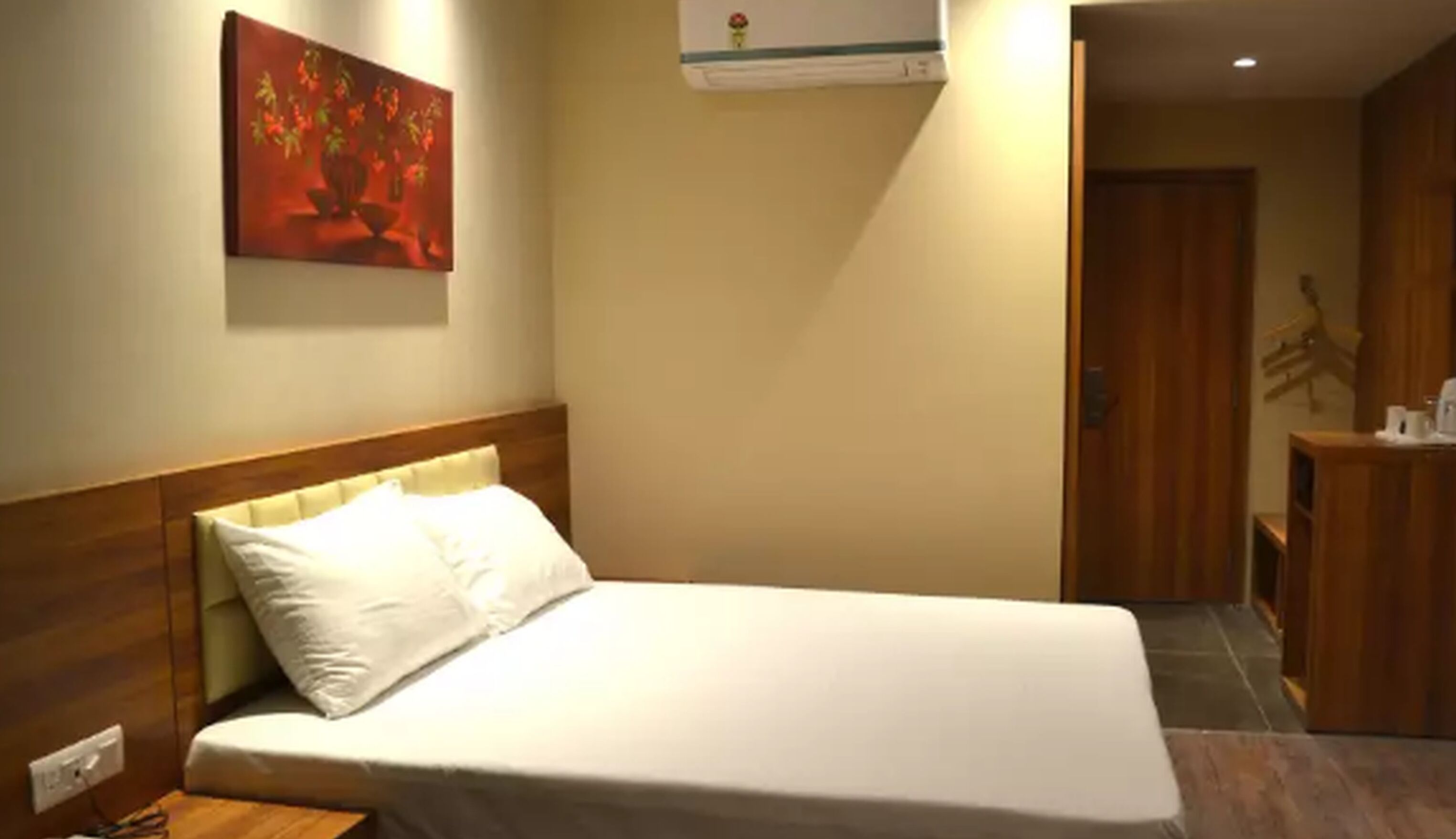 A hotel room with a bed, a painting on the wall, and a wooden door.