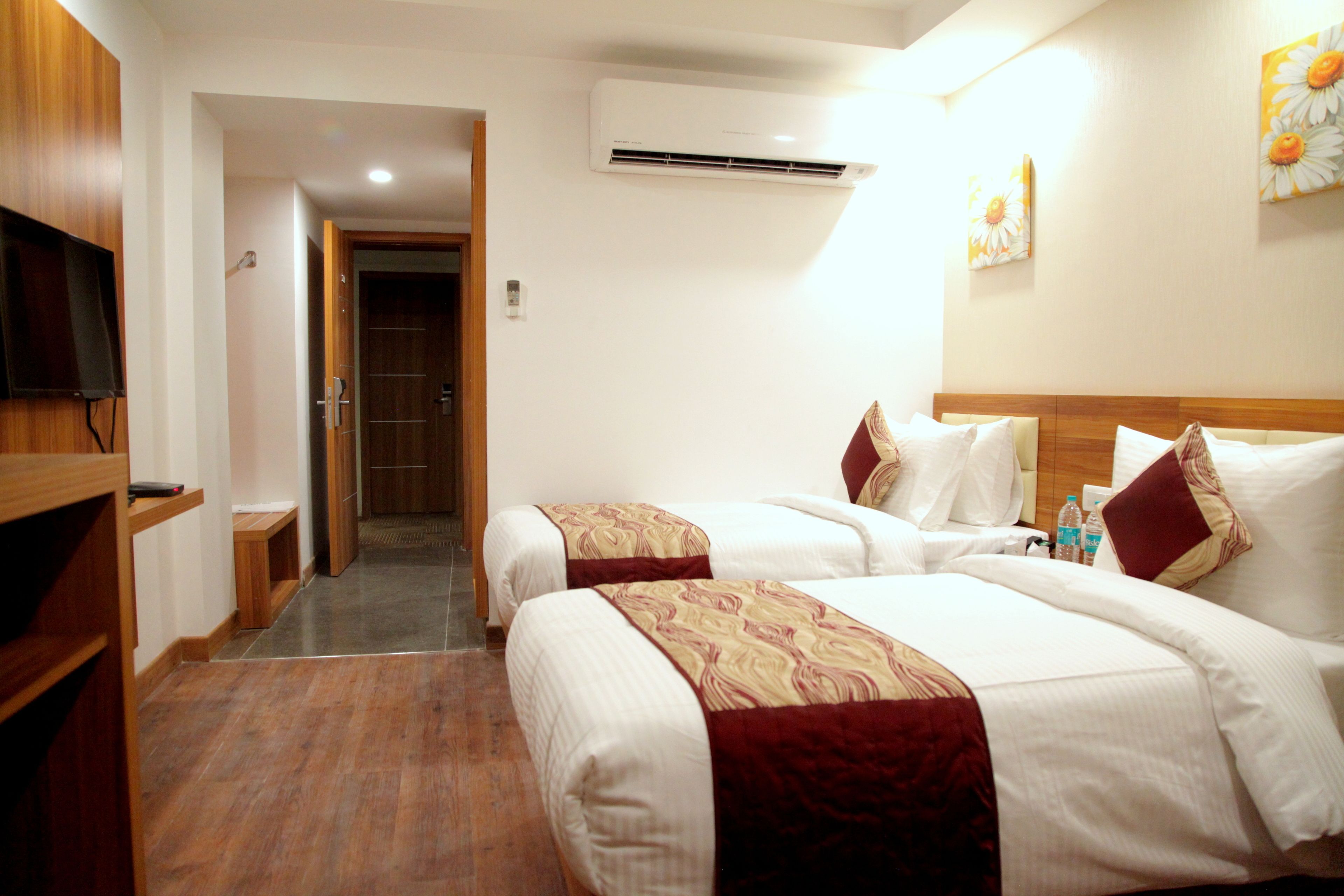Habitación de hotel con dos camas, televisión, aire acondicionado y un pasillo que conduce a otra habitación.