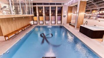 A swimming pool with a hot tub, benches, and a view of giraffes through the glass enclosure.