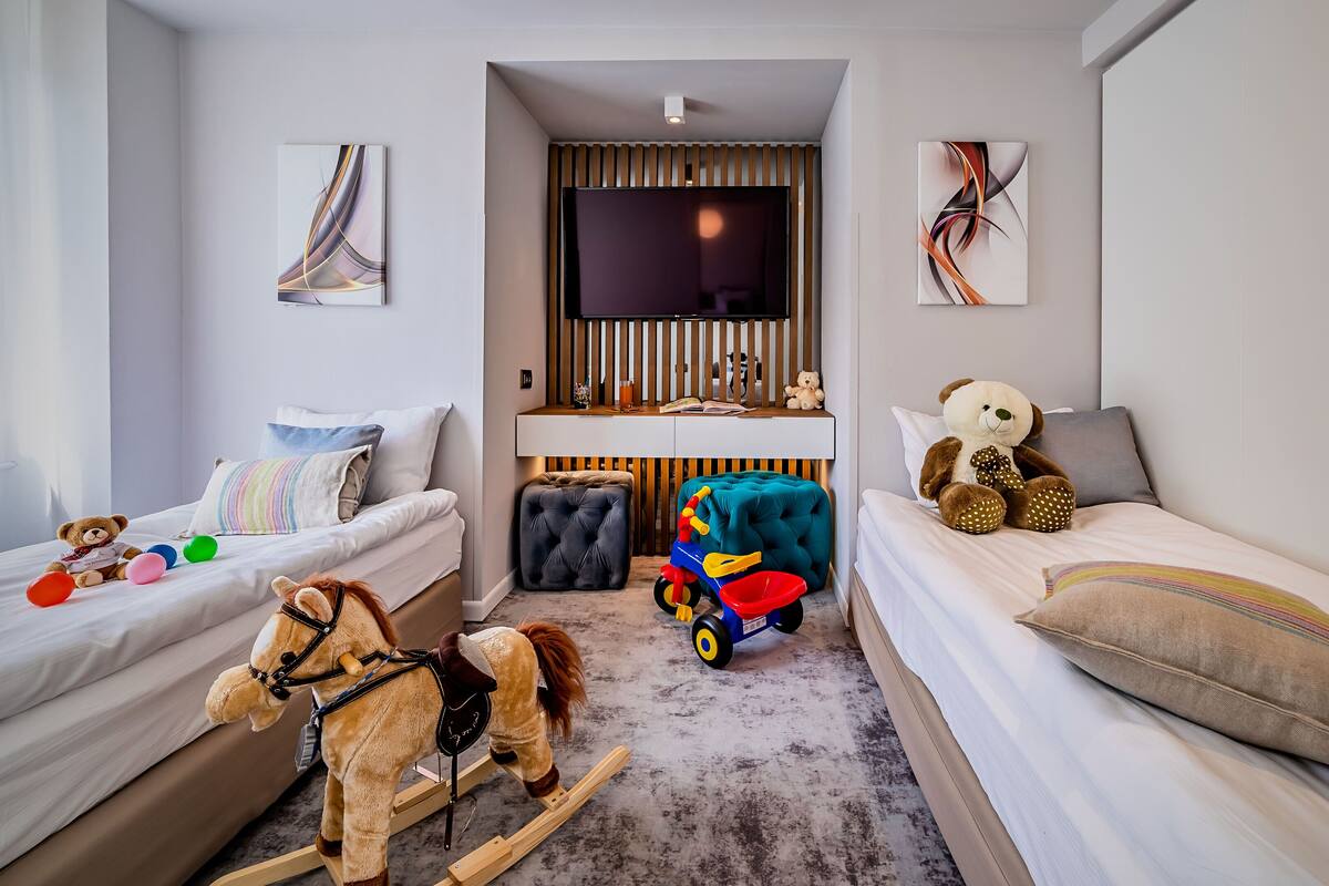 A child's bedroom with two beds, a rocking horse, a toy car, and a teddy bear.