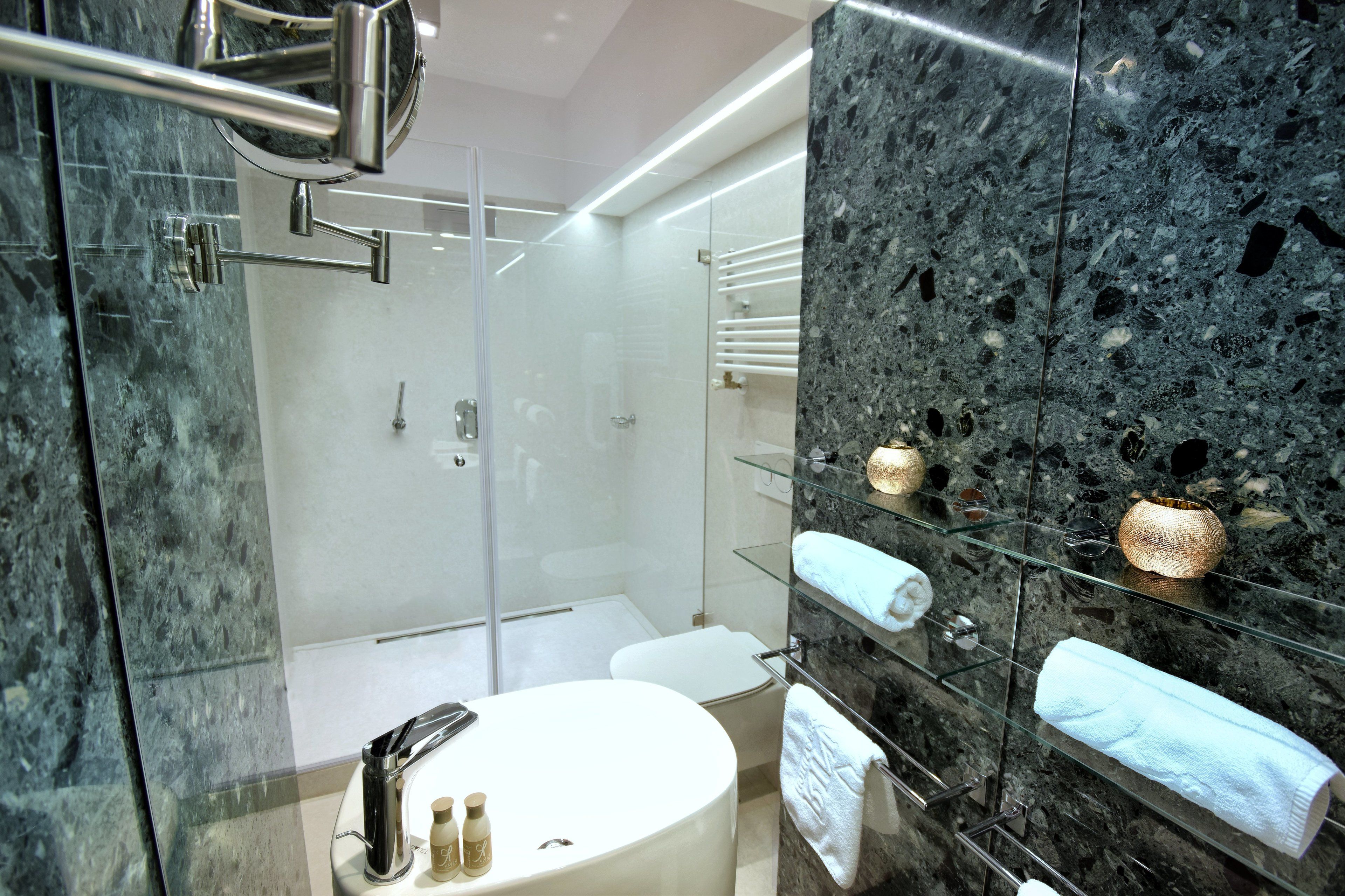 A modern bathroom with a glass-enclosed shower, a white sink, and marble walls.