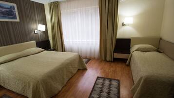Habitación de hotel con dos camas, suelo de madera, ventana con cortinas traslúcidas, aire acondicionado instalado en la pared y un cuadro en la pared.