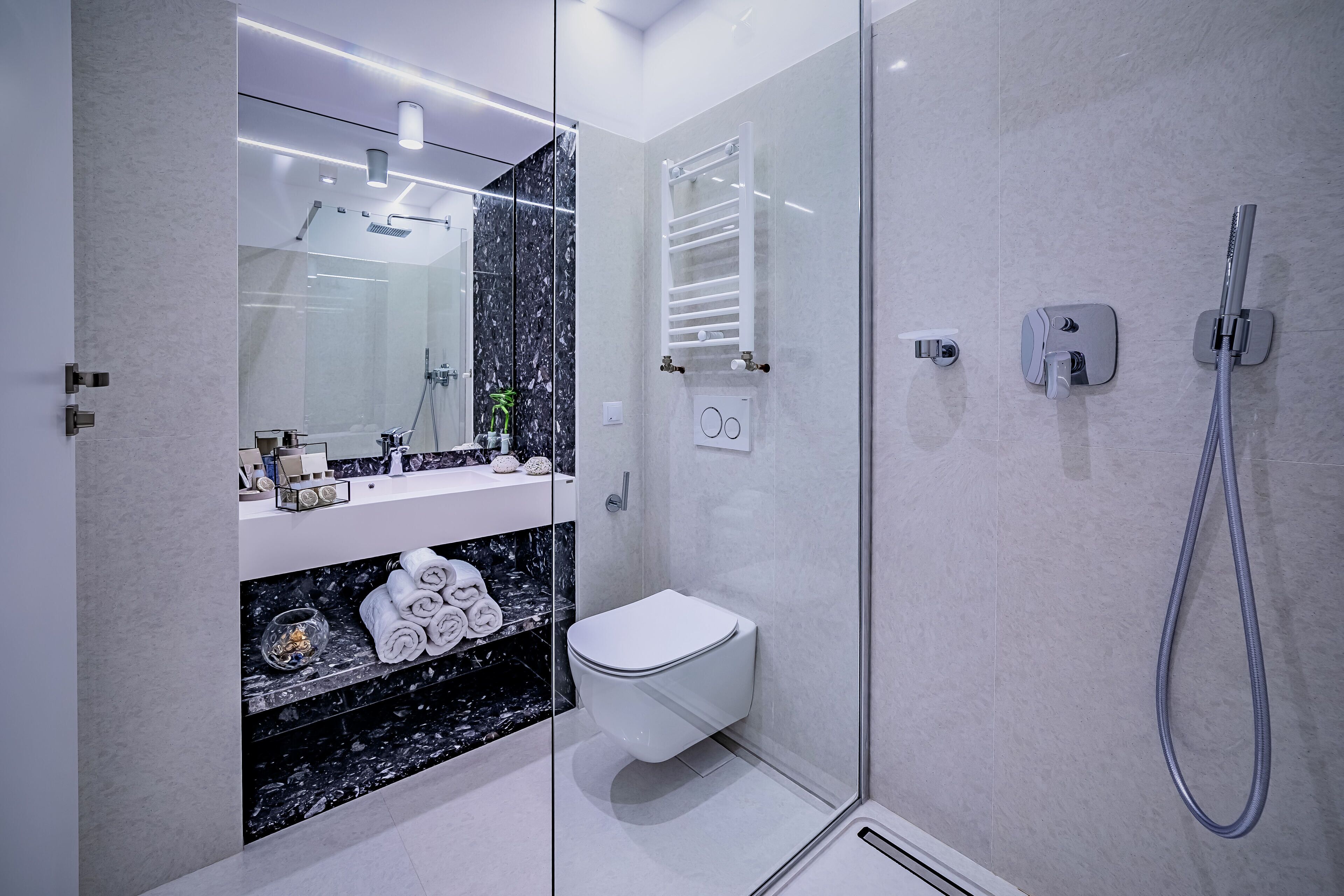 Un baño moderno con cabina de ducha de vidrio, inodoro blanco y encimera de mármol con toallas.
