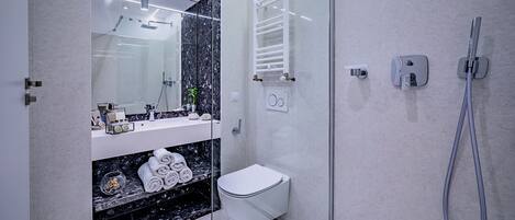 Un baño moderno con cabina de ducha de vidrio, inodoro blanco y encimera de mármol con toallas.