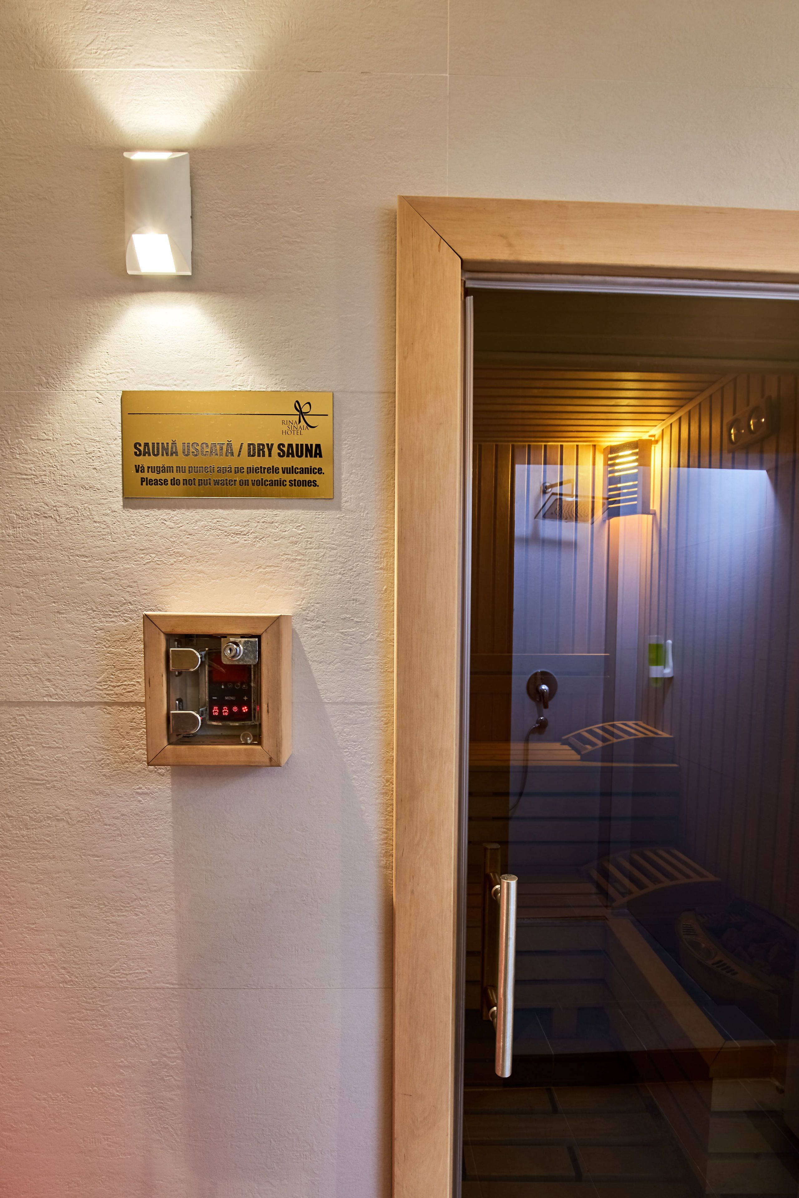 Entrada a una sauna seca con puerta de madera, panel de control y cartel con el nombre y las instrucciones de la sauna.