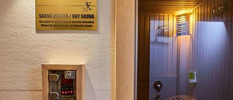 Entrada a una sauna seca con puerta de madera, panel de control y cartel con el nombre y las instrucciones de la sauna.