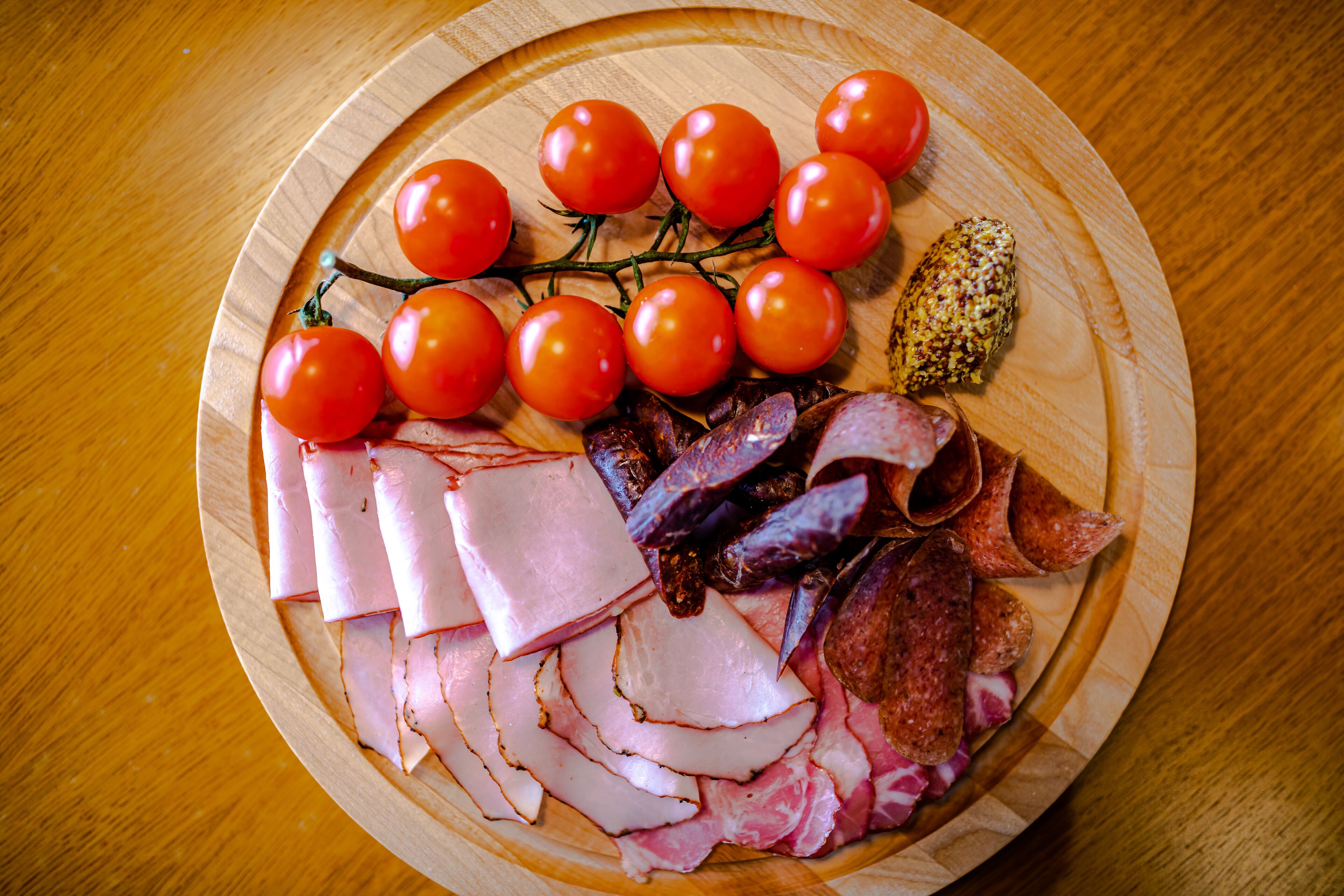 Una bandeja de madera con carnes cortadas, tomates cherry y un trozo pequeño de queso.