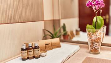 A bathroom with a towel, bottles of essential oils, and a glass vase with a flower.