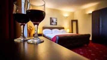 Two wine glasses on a table with a bed and a nightstand in the background.
