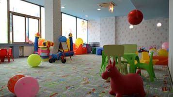 A brightly lit indoor play area with colorful play structures, a large window, and a patterned floor.