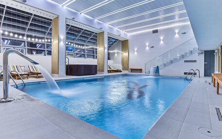 An indoor swimming pool with a clear water view, a modern ceiling design, and a staircase leading to an upper level.