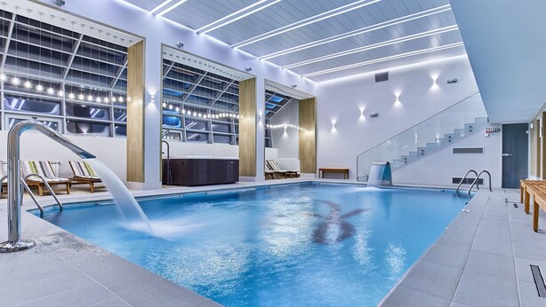 An indoor swimming pool with a clear water view, a modern ceiling design, and a staircase leading to an upper level. - Hotel Sinaia (Sinaia)