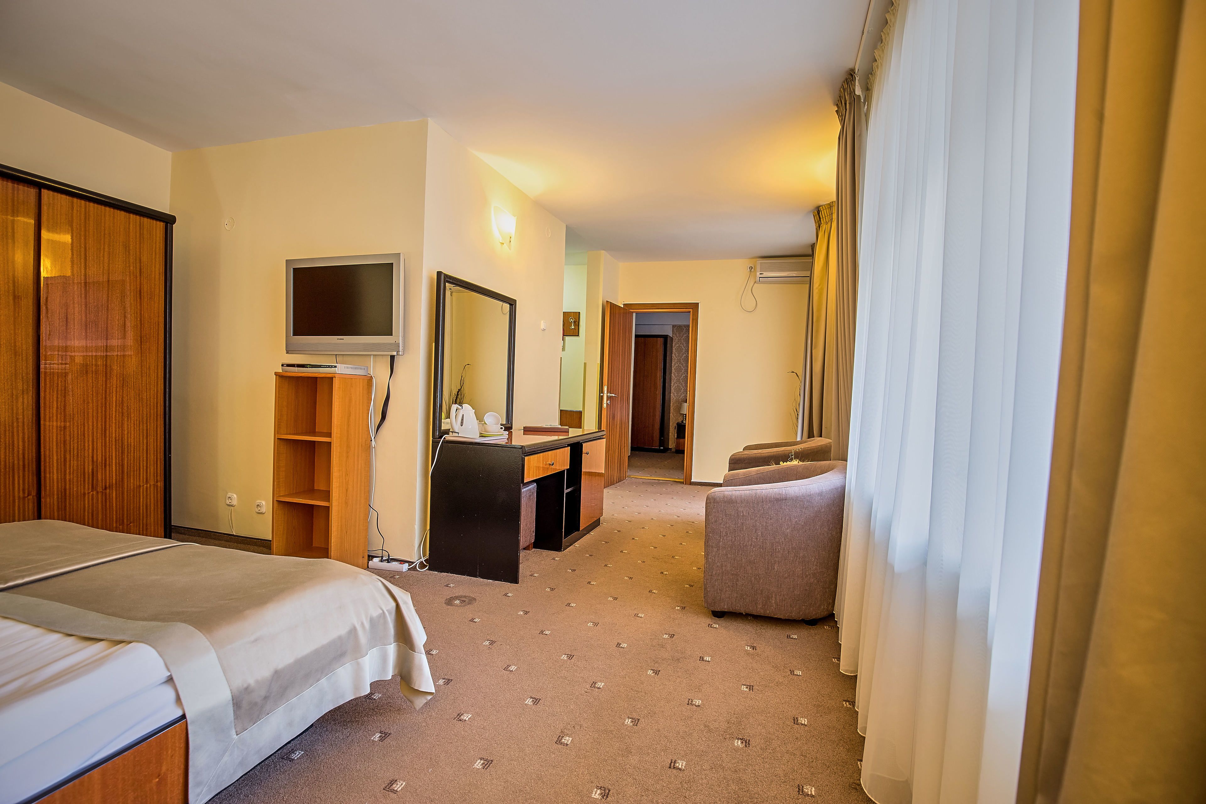 A hotel room with a bed, a desk with a computer, a television, a mirror, and a chair.