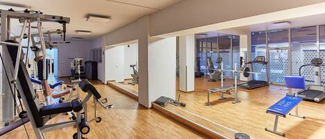 A gym with cardio machines, free weights, and a mirrored wall.