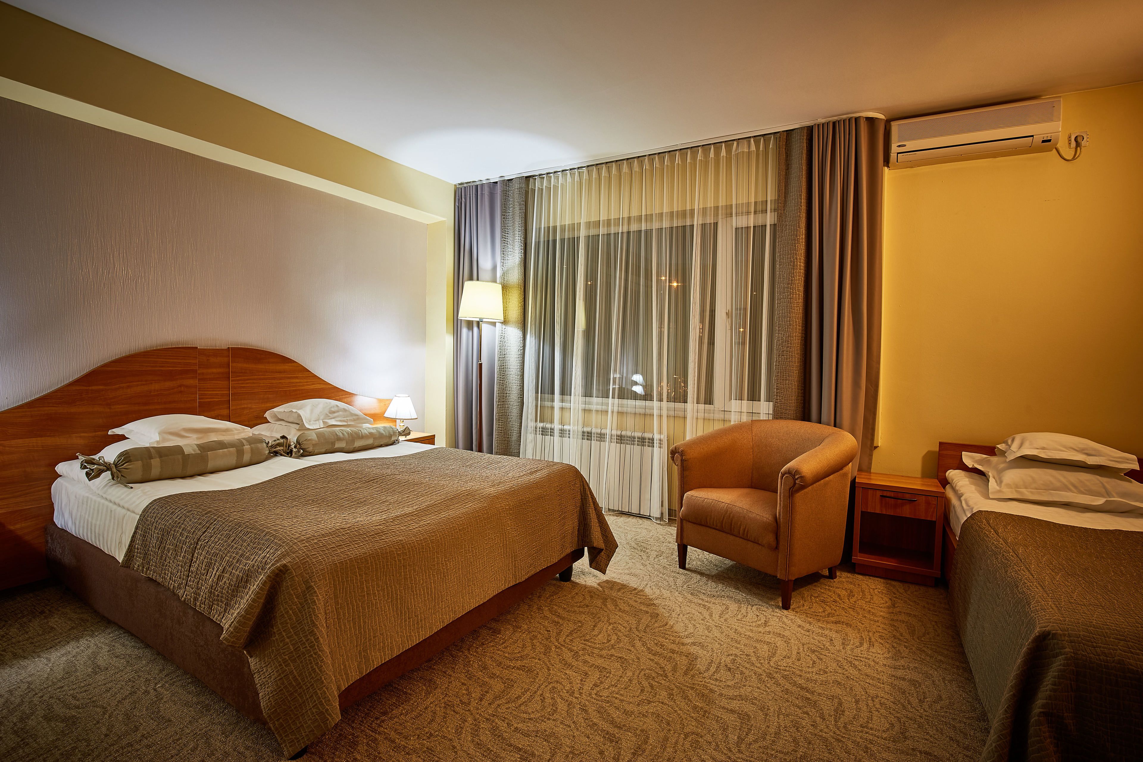 Une chambre d’hôtel avec un grand lit, une chaise, une table de chevet et une fenêtre avec des rideaux.