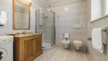 Un baño con ducha de vidrio, tocador de madera, inodoro y lavamanos.