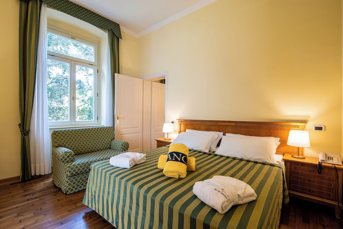 Ein Hotelzimmer mit einem großen Bett, einem Sofa, einem Nachttisch mit Lampe und einem Fenster mit Vorhängen.