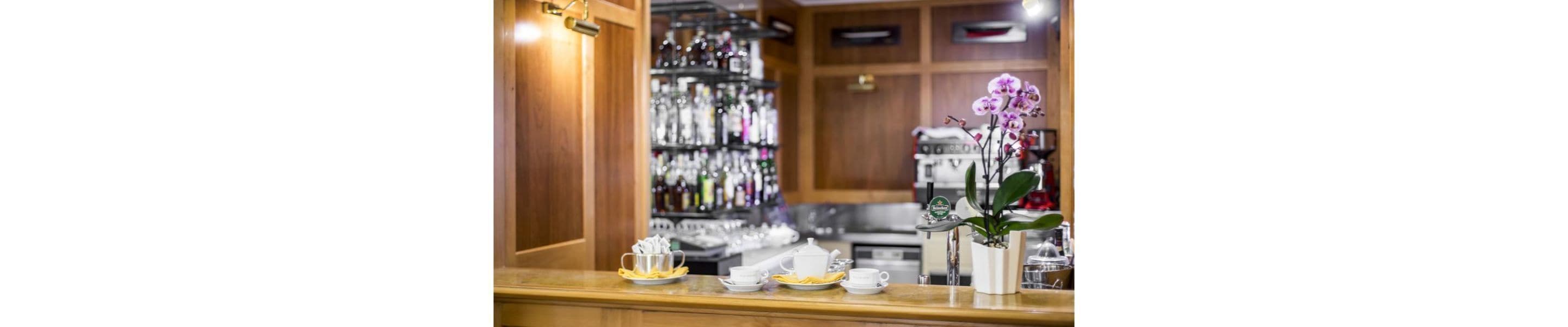 A bar area with a wooden counter, a shelf with bottles, and a potted orchid.