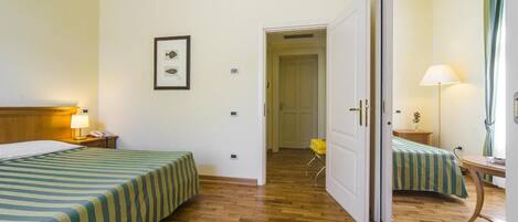 Une chambre d’hôtel avec deux lits, un bureau, une chaise et une porte donnant sur une autre pièce.